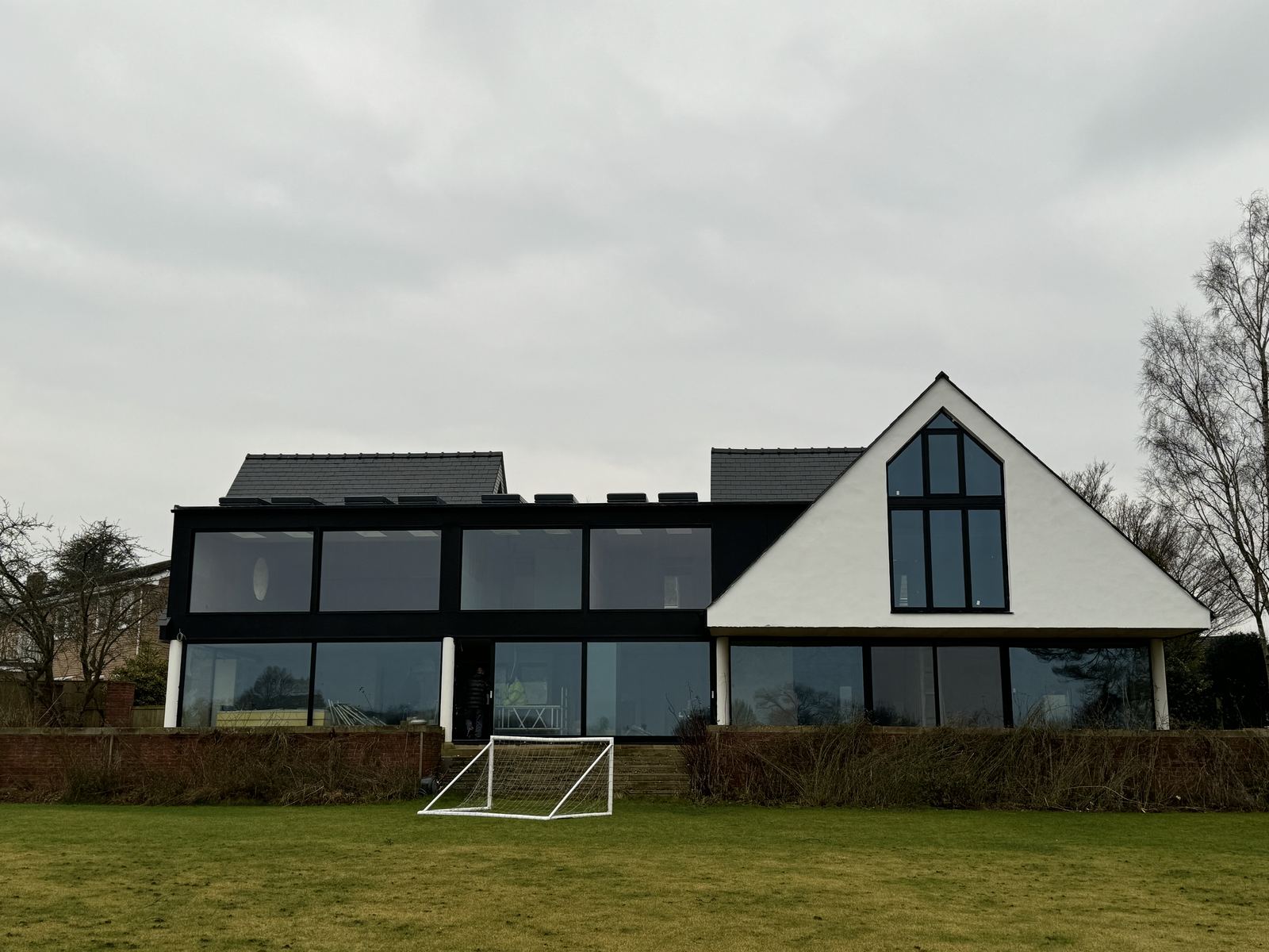 Completed contemporary house with full-height dark-framed glazing and a white rendered gable